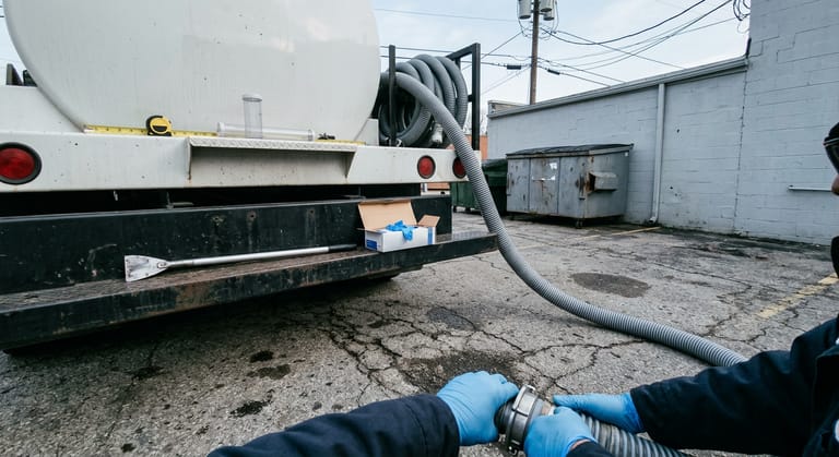 Rear of an unmarked vacuum truck with a four inch suction hose, scraper and gloves on the bumper